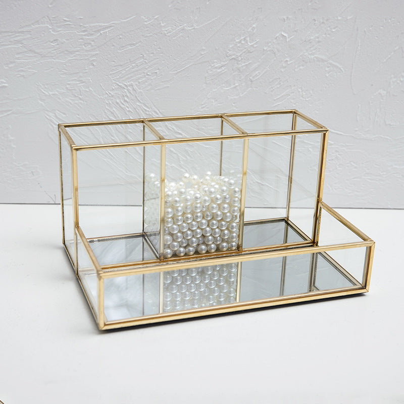Glass makeup organizer with gold metal frame displayed upright, showing compartments for brushes and beauty products on a bat