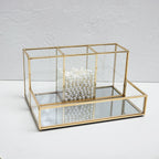 Glass makeup organizer with gold metal frame displayed upright, showing compartments for brushes and beauty products on a bat