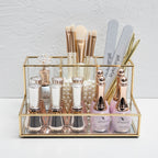Glass makeup organizer with gold metal frame displayed upright, showing compartments for brushes and beauty products on a bat