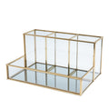 Glass makeup organizer with gold metal frame displayed upright, showing compartments for brushes and beauty products on a bat