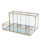 Glass makeup organizer with gold metal frame displayed upright, showing compartments for brushes and beauty products on a bat
