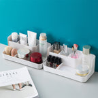 Clear desktop makeup organizer with 5 compartments holding brushes, lipsticks, and skincare products on a vanity